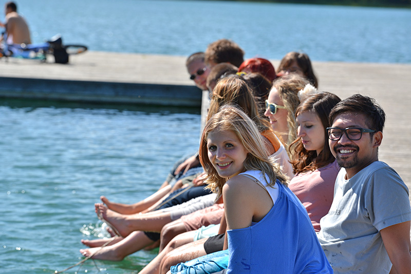 Studierende sitzen auf einem Steg am See