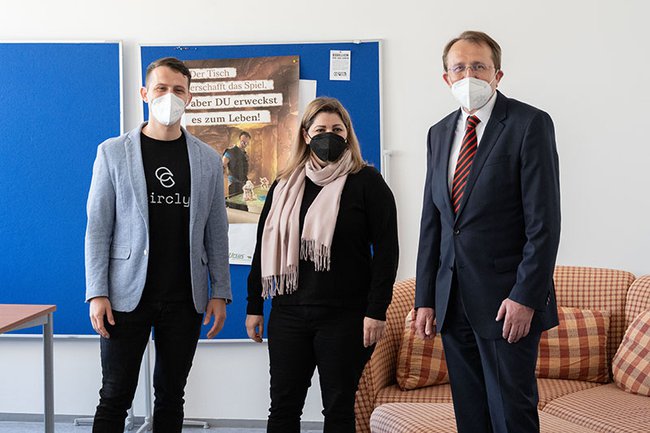 Wir sehen drei Menschen - eine Frau und zwei Männer, sie stehen vor einem Plakat und tragen FFP2 Masken. Es handelt sich um Lydia Popp von Loonity, Eric Weisz von Circly und Bürgermeister Matthias Stadler