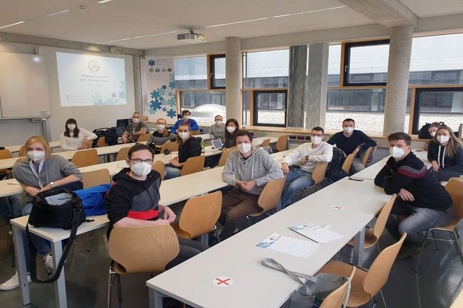 Die Teilnehmen des Kurses sitzen - mit FFP2 Masken und Abstand - im Seminarraum und schauen in die Kamera