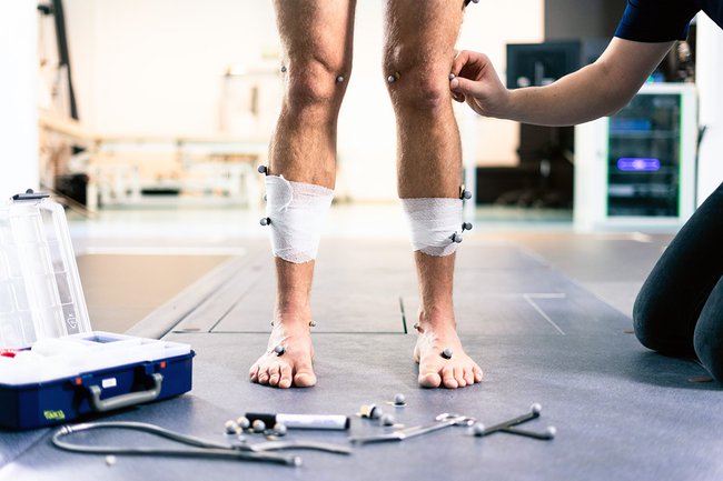 Ein Proband bekommt Sensoren zur Bewegungsanalyse auf die Beine geklebt