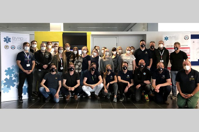 Gruppenfoto der Studierenden und Lehrenden des notfallmedizinischen Spezialkurses in einem Seminarraum neben Aufstellern des BVRD (Bundesverband Rettungsdienst) – alle tragen FFP2 Masken