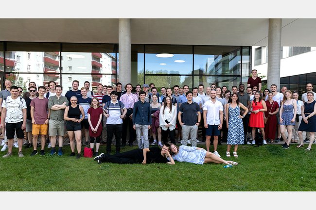 Eine große Gruppe von lächelnden Studierenden (ca. 60 Personen) auf der Wiese vor der Fachhochschule St. Pölten