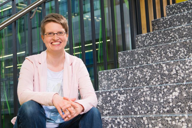 Kerstin Blumenstein sits on the stair of the main building of St. Pölten UAS and smiles into the camera